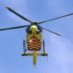 mentőhelikopter repül a sárga gépen piros csíkok vannak felette az enyhén felhős kék ég és látszik a rotor