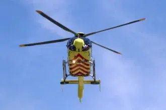 mentőhelikopter repül a sárga gépen piros csíkok vannak felette az enyhén felhős kék ég és látszik a rotor