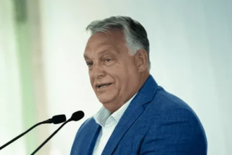 Orbán Viktor kötcse beszél bejelentés kék öltönyben mikrofon előtt fehér ingben beszél és nevet