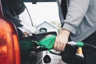 tankol üzemanyag férfi töltőpisztolyt tart a kezében szürke pulóverben a sötét autó mellett