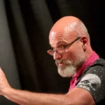 Zacher Gábor pólóban szemüvegben mutogat