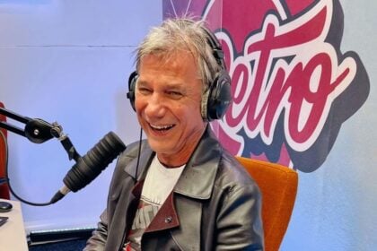 Bochkor Gábor kabátban fehér pólóban mikrofon előtt fejhallgatóval a fülén nevet