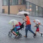 esőben sétáló anya és gyerekek a kezükben esernyő zivatar közben