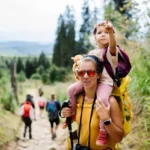 Családi kirándulás felnőtt nő nyakában gyerek háttérben zöld fák és emberek