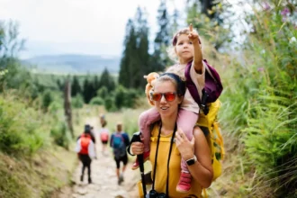 Családi kirándulás felnőtt nő nyakában gyerek háttérben zöld fák és emberek
