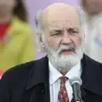 Iványi Gábor szakállal fekete zakóban kopaszodó hajjal beszél fehér ingben mögötte emberek ülnek