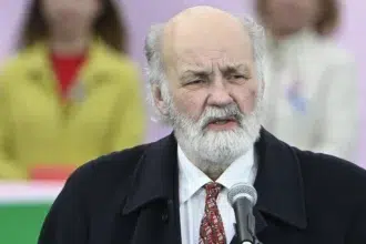 Iványi Gábor szakállal fekete zakóban kopaszodó hajjal beszél fehér ingben mögötte emberek ülnek