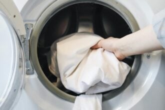 egy kéz a mosógépbe dobálja be a ruhákat