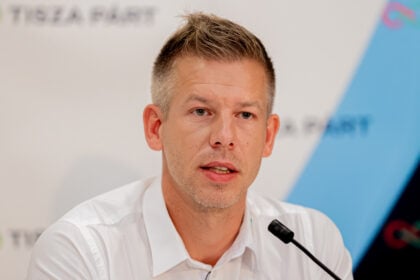 Magyar Péter fehér ingben ül egy mikrofon előtt