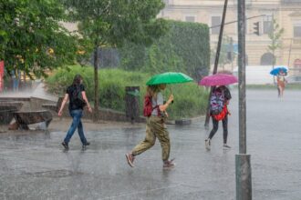 Fiatalok futnak az esőben színes esernyőkkel a város közepén - heves nyári zápor utcai jelenet zöld, rózsaszín és kék esernyőkkel