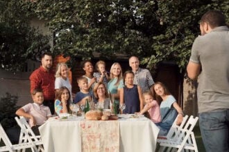 A képen egy nagyobb család látható egy vidám, tavaszi képen, miközben egy fotós képet készít róluk.