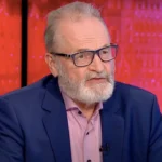 Farkas András nyugdíjszakértő kék zakóban szemüvegben egy tévéstúdióban rózsaszín ingben beszél