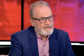 Farkas András nyugdíjszakértő kék zakóban szemüvegben egy tévéstúdióban rózsaszín ingben beszél