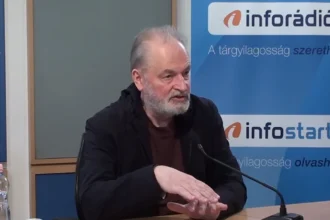Farkas András fekete zakóban, barna pólóban, mikrofonba beszél az Inforádió stúdiójában egy asztalnál.