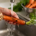 Egy ember kefével mossa a földdel szennyezett sárgarépát.