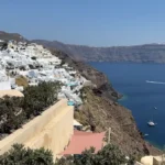 A képen Szantorini szigetének egy részlete látható nagy, kopár sziklákkal és fehér házakkal.