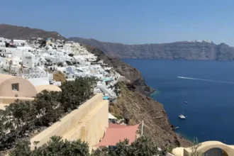A képen Szantorini szigetének egy részlete látható nagy, kopár sziklákkal és fehér házakkal.