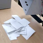 Egy szavazóurnából öntenek ki szavazólapokat egy faasztalra.