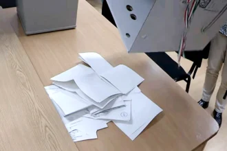 Egy szavazóurnából öntenek ki szavazólapokat egy faasztalra.