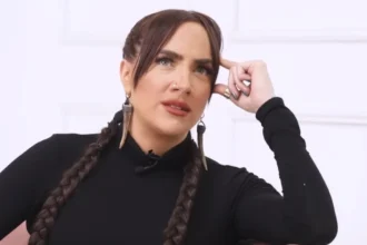 Tóth Gabi fekete felsőben, befont barna hajjal, erős sminkben enyhén balra és felfelé néz fehér háttér előtt.